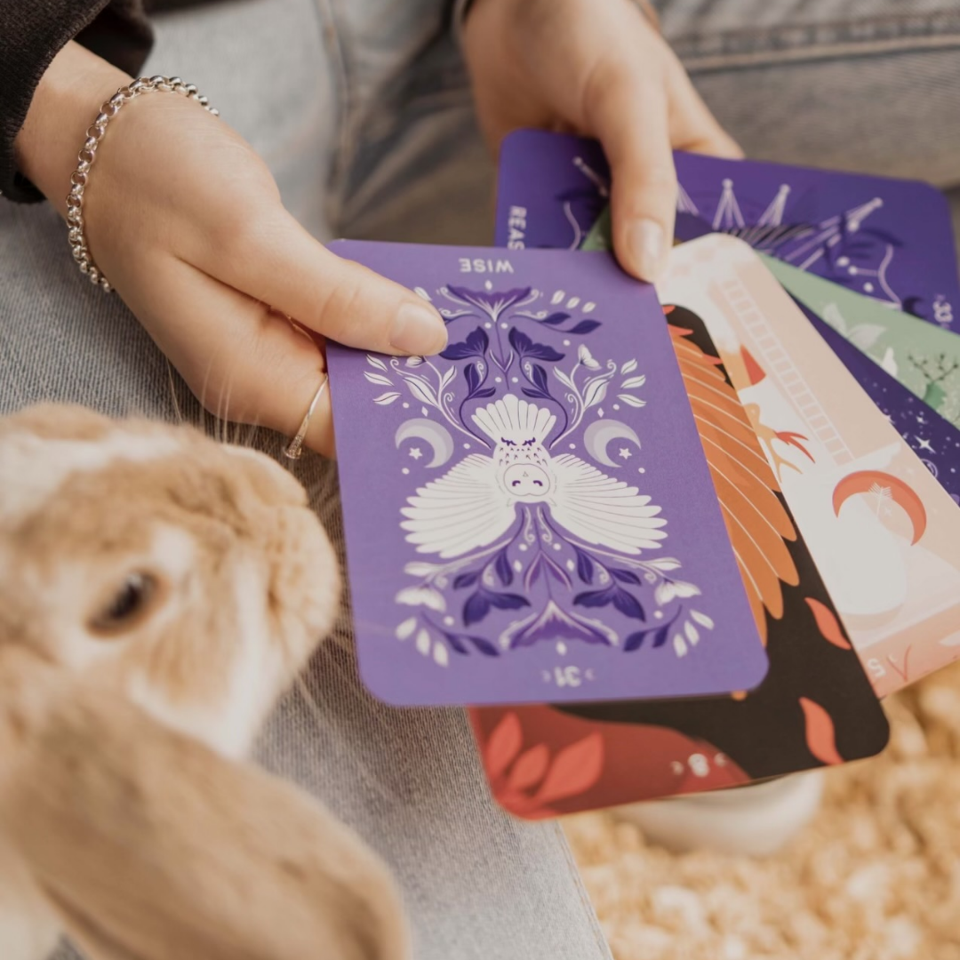 A person holding a set of colorful oracle or tarot cards with intricate, artistic designs
